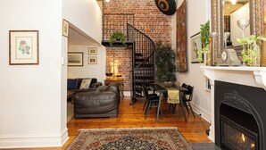 A cozy living room with a fireplace, a dining area, and a staircase against a brick wall. - Luxury mansion loft by the beach (St kilda west)