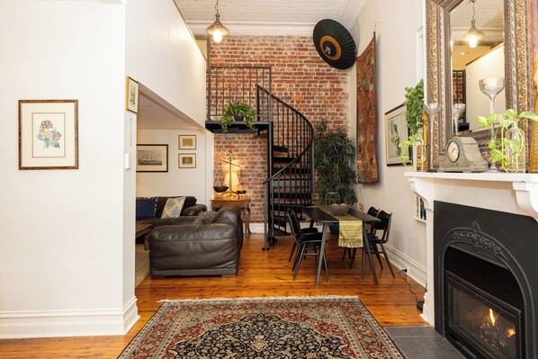 Un salon chaleureux avec une cheminée, un coin repas et un escalier adossé à un mur de briques.