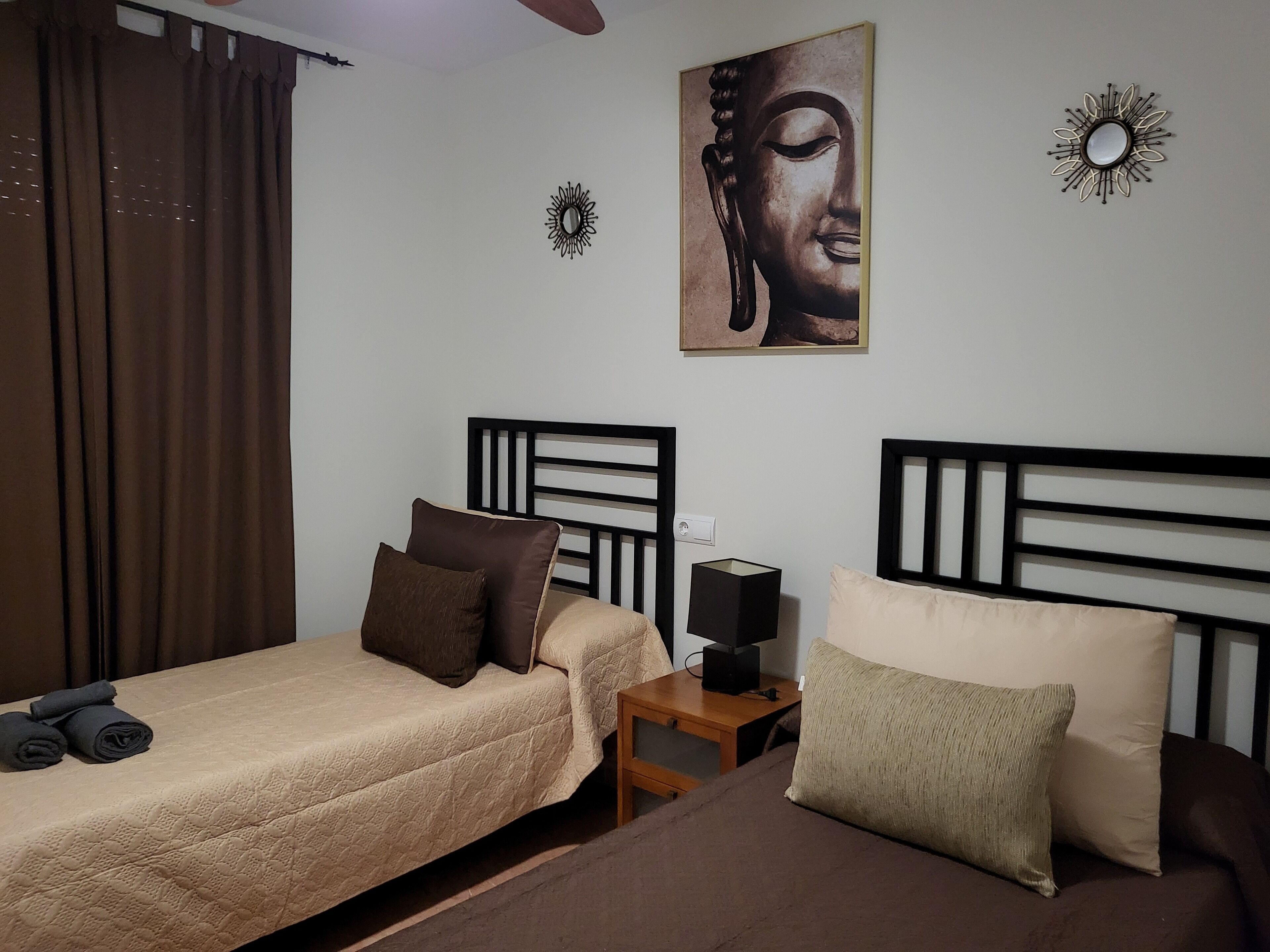 A bedroom with two beds, a nightstand, a wall-mounted mirror, and a Buddha painting.