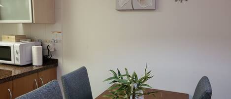 Un comedor con una mesa de madera, sillas estampadas, una planta en maceta, un microondas y un cuadro de flores colgado en la pared.