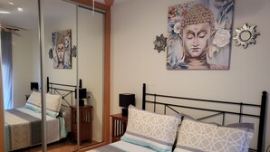 A neatly made bed with patterned bedding, a bedside table with a lamp, and a wall with a Buddha painting and decorative mirrors. - Relaxing essence bass with private pool and patio! (Vera)