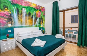 A hotel room with a large bed, a nightstand, a small table with a chair, a view of a balcony, and a painting of a waterfall. - Lovely Bed and Breakfast in Center of Sorrento (Sorrento)
