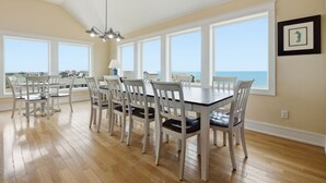 A dining area with a table and chairs, large windows, and a view of the ocean. - Hatteras Retreat Oceanfront Home + Pets Stay Free (Buxton)