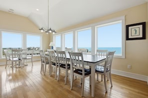 Een eethoek met een tafel en stoelen, grote ramen en uitzicht op de oceaan.