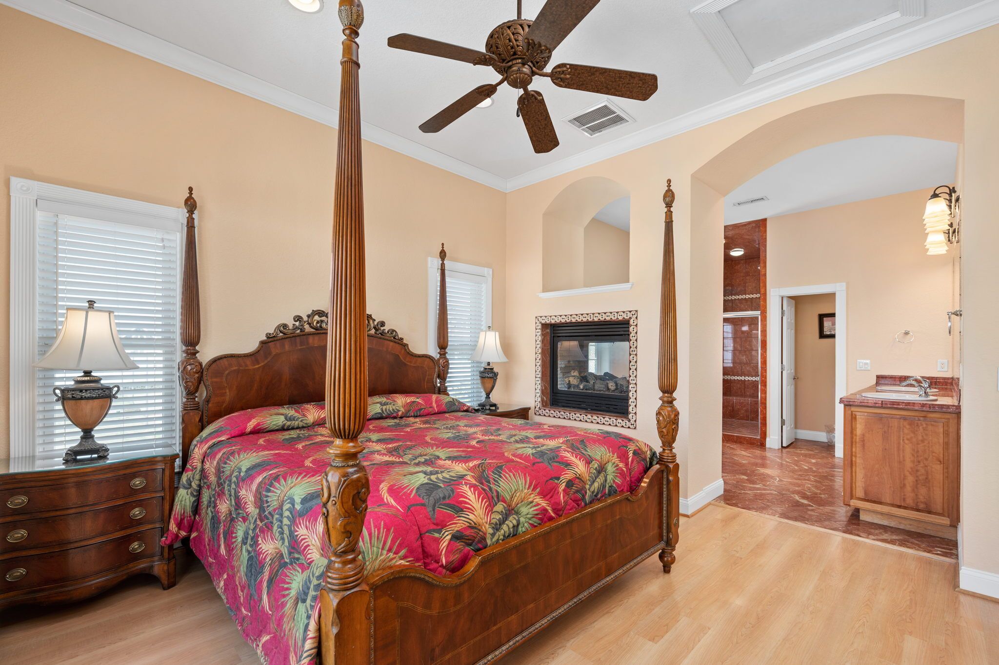 A spacious bedroom with a four-poster bed, a ceiling fan, and a fireplace.