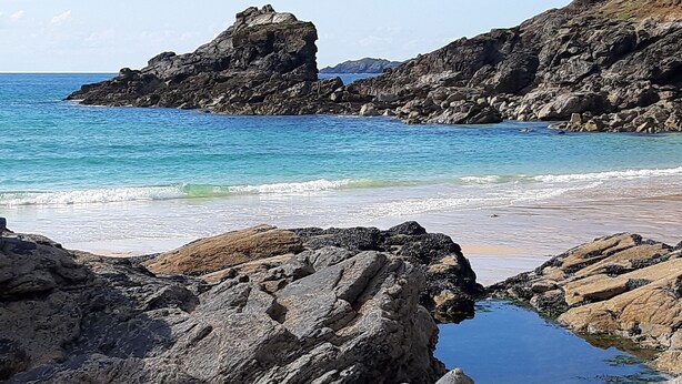 A rocky coastline with clear blue waters and a small pool of water in the foreground.