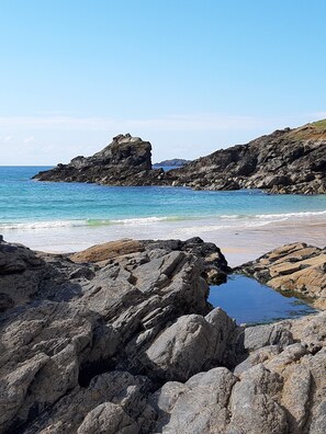 A rocky shoreline with clear blue water and a distant view of a rugged coastline. - Glebe Cottage, Little Petherick, near Padstow (Little Petherick)