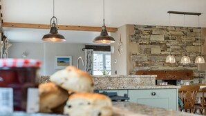 A kitchen with a stone wall, wooden beams, and pendant lighting.