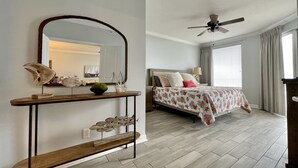 A bedroom with a bed, a ceiling fan, a bedside table with decorative items, and a large mirror. - PCB - Marisol - Spring and Summer Dates Available!!  Discounted Rates!! (Panama City Beach)