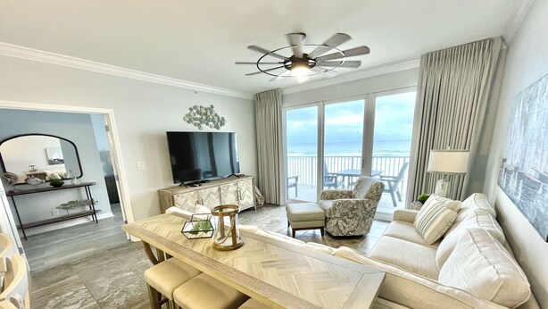 A modern living room with a sofa, a dining table with bar stools, a television, and a view of the ocean through large windows. - PCB - Marisol - Spring and Summer Dates Available!!  Discounted Rates!! (Panama City Beach)