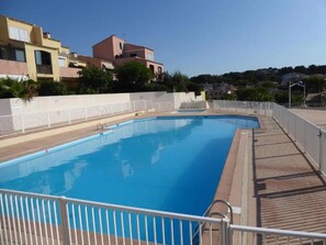 A swimming pool with a wooden deck and white railing.