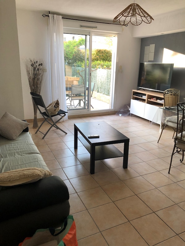 A living room with a sofa, a coffee table, a TV, and a sliding glass door leading to a garden.
