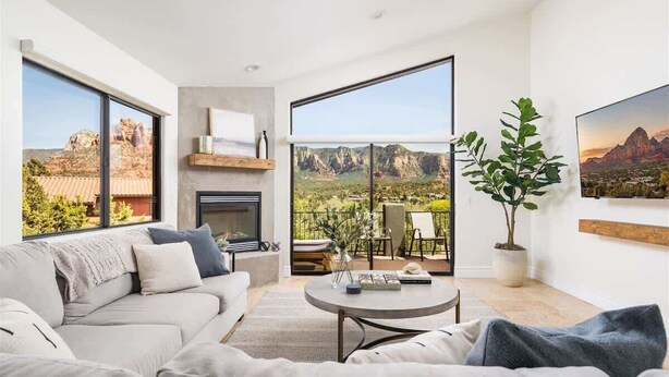 A modern living room with a sofa, coffee table, and a fireplace. There is a balcony with a view of mountains. - Upscale Red Rock Retreat- Spa, Views, Pet Friendly (Sedona)