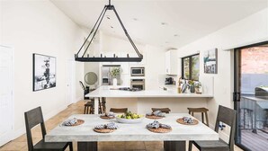 A modern kitchen with a central island, white cabinetry, and a dining area with a large table and chairs. - Upscale Red Rock Retreat- Spa, Views, Pet Friendly (Sedona)