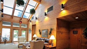 A cozy indoor area with wooden walls, a sofa, chairs, and a table with lamps. There is a door with a sign and a window with a view outside.