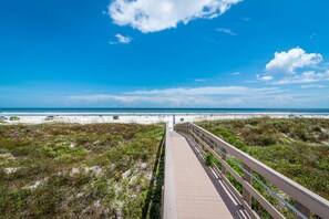 A boardwalk leading to a beach with dunes and a clear sky.