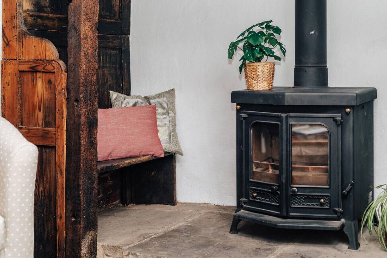 A cozy room with a black wood-burning stove, a wooden bench with cushions, and a potted plant.