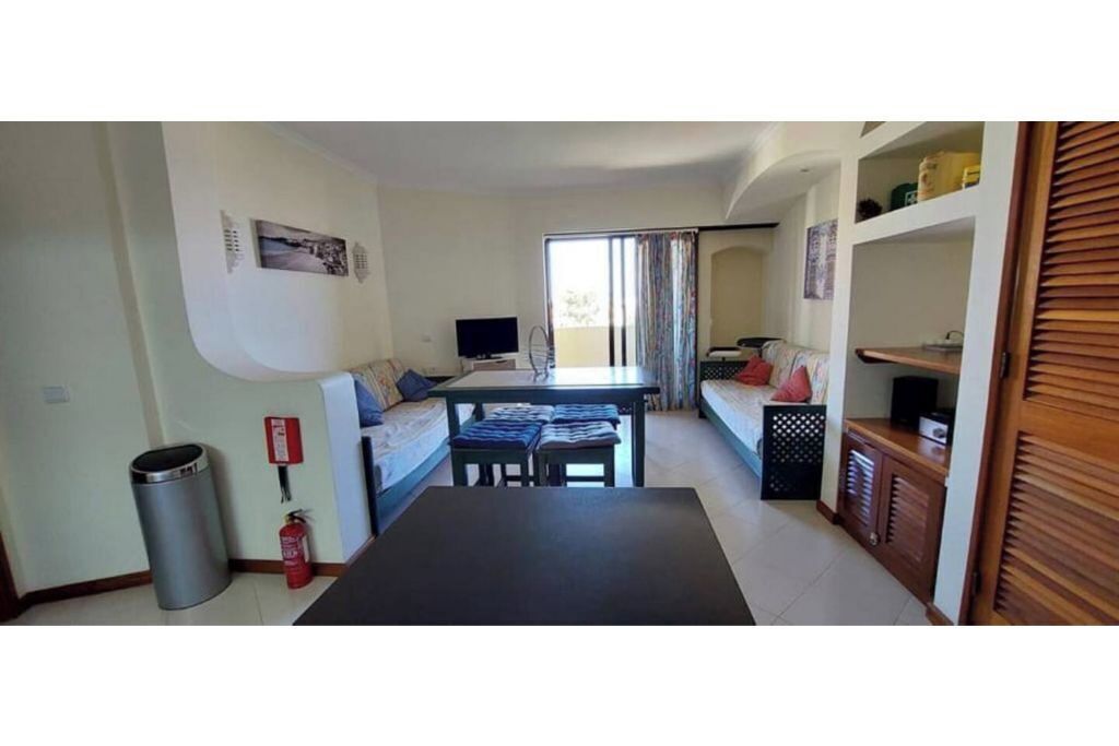A compact living space with a sofa, a small dining table, a TV, and a trash bin.