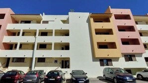 Un immeuble résidentiel à plusieurs étages, doté de balcons, un espace de stationnement avec plusieurs voitures et un ciel bleu dégagé.