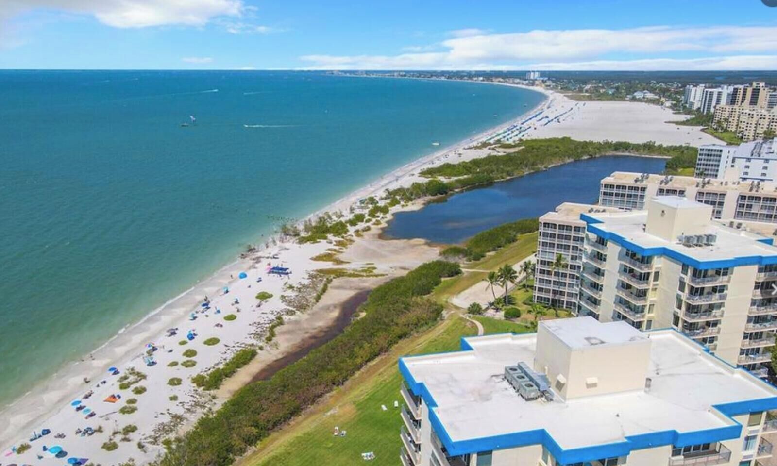 A coastal hotel with multiple high-rise buildings, a beach with umbrellas, and a marina.
