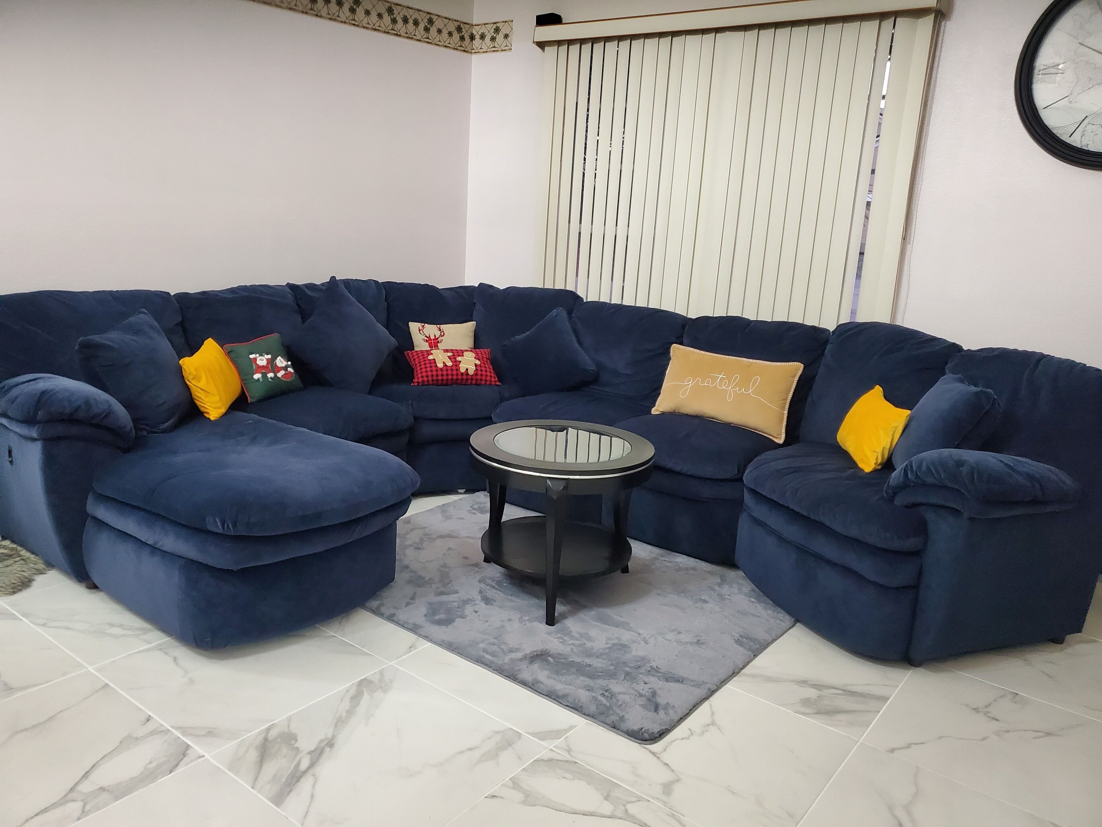 A blue sectional sofa with multiple cushions, a small round table, and a grey rug.