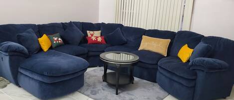 A blue sectional sofa with multiple cushions, a small round table, and a grey rug.