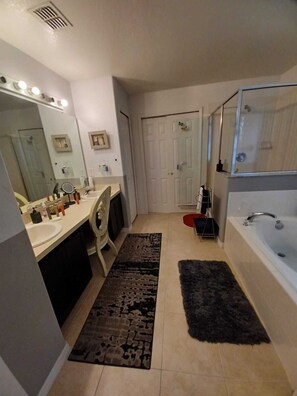 Une salle de bain moderne avec un meuble-lavabo à deux vasques, un grand miroir, une cabine de douche et un tapis foncé sur le sol.