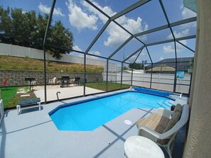 Une piscine extérieure couverte offrant une vue dégagée sur les environs, ainsi qu’une terrasse avec des chaises et un barbecue.
