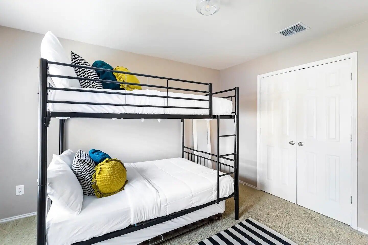 Une chambre avec un lit superposé, dotée de draps blancs et d’oreillers colorés.