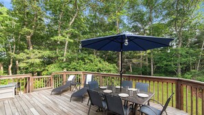 A wooden deck with a table and chairs, surrounded by trees. - Minutes to Bayside Beaches, Dogs Welcome! (Eastham)