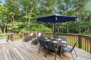 A wooden deck with a table and chairs, surrounded by trees. - Minutes to Bayside Beaches, Dogs Welcome! (Eastham)