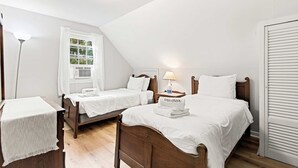 A room with two wooden beds, a nightstand with a lamp, a window with curtains, and a white wardrobe.