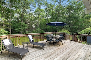 A wooden deck with a table and chairs, surrounded by trees. - Minutes to Bayside Beaches, Dogs Welcome! (Eastham)