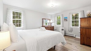 A bedroom with a large bed, two windows with curtains, a dresser, a mirror, and a lamp. - Minutes to Bayside Beaches, Dogs Welcome! (Eastham)