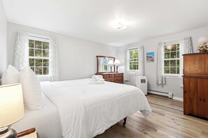A bedroom with a large bed, two windows with curtains, a dresser, a mirror, and a lamp. - Minutes to Bayside Beaches, Dogs Welcome! (Eastham)