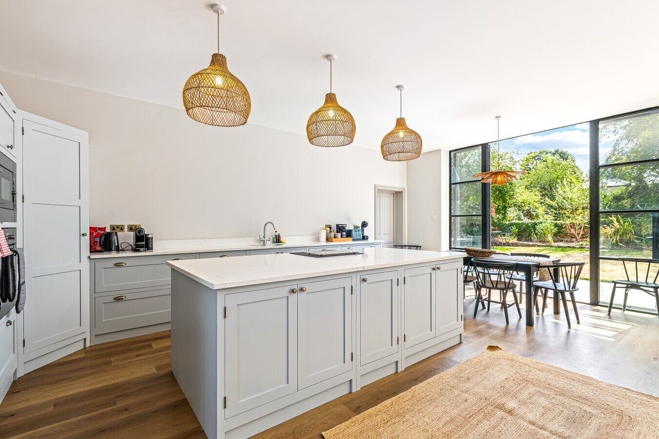 Een moderne keuken met een groot eiland, witte kasten en drie hangende wilgentwillichtjes.