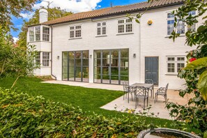 Un edificio blanco con amplias ventanas, una puerta y un pequeño patio con mesa y sillas.