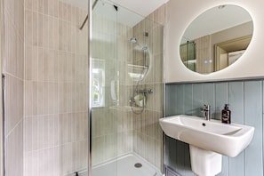 Une salle de bain moderne avec une douche à parois de verre, un lavabo blanc et un miroir rond.