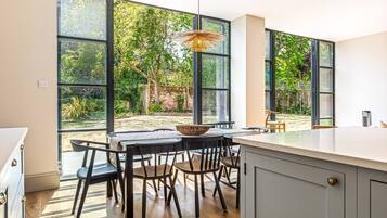 A modern kitchen with large windows, a dining area with chairs and a table, and a hanging light fixture.