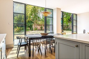 A modern kitchen with large windows, a dining area with chairs and a table, and a hanging light fixture. - Montpellier House, Centrally Located, Pet Friendly (Henley-On-Thames)