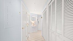 A hallway with white doors, a small table with a lamp, and a mirror on the wall. - Watch the Fireworks From Your Balcony!!! (Ocean City)