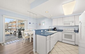 A modern kitchen with white cabinets, a blue countertop, and a large window overlooking a balcony. - Watch the Fireworks From Your Balcony!!! (Ocean City)