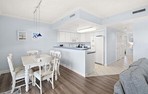 A modern kitchen with white cabinets, a central island, and a dining area with white chairs. - Watch the Fireworks From Your Balcony!!! (Ocean City)