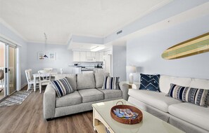 A modern living room with a grey sofa, a white sofa, and a coffee table with magazines. There is a dining area with a white table and chairs, and a kitchen in the background. - Watch the Fireworks From Your Balcony!!! (Ocean City)