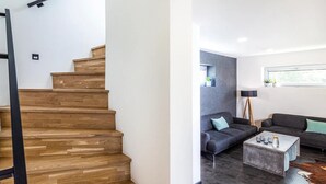 A modern living room with a staircase, a grey sofa, a coffee table, and a window with plants. - Fr Dlant Mcmp525 in Fr Dlant nad Ostravic (Frydlant nad Ostravici)