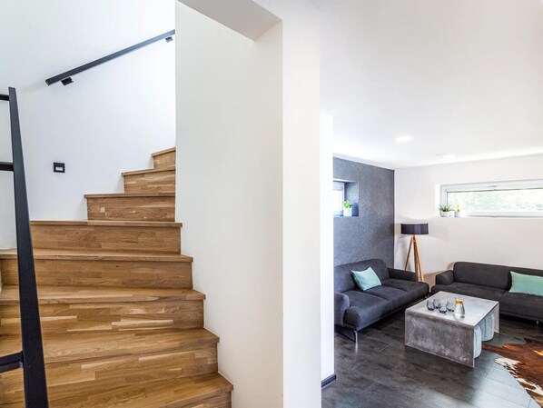A modern living room with a staircase, a grey sofa, a coffee table, and a window with plants. - Fr Dlant Mcmp525 in Fr Dlant nad Ostravic (Frydlant nad Ostravici)