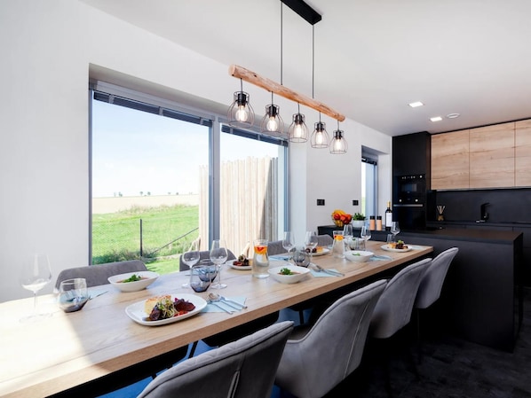 A modern dining area with a long wooden table set for a meal, large windows offering a view of the outdoors, and a minimalist kitchen in the background. - Fr Dlant Mcmp525 in Fr Dlant nad Ostravic (Frydlant nad Ostravici)