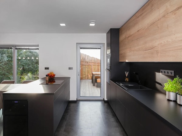 Cucina moderna con mobili scuri, una parete a parete in legno e vista su un terrazza in legno.