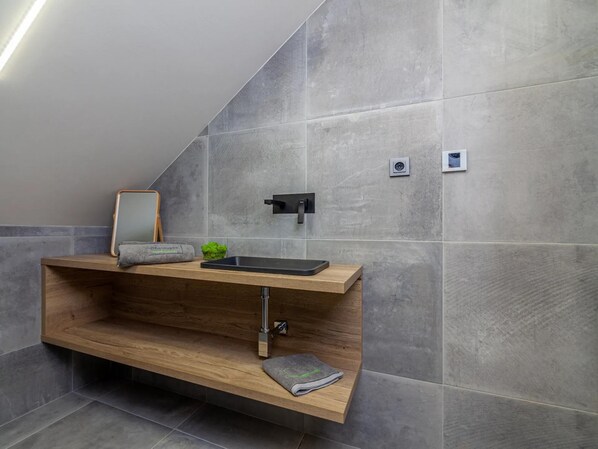 A modern bathroom with a wooden vanity, a black sink, and a mirror.