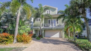 Uma casa de dois andares com garagem, cercada por palmeiras e plantas tropicais.